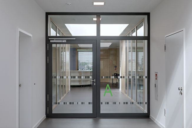 Elektromos rögzítőszerkezettel rendelkező GEZE TS 5000 R felső szerelésű ajtócsukó füstkapcsolóval a folyosón a rheinhauseni általános iskolában.