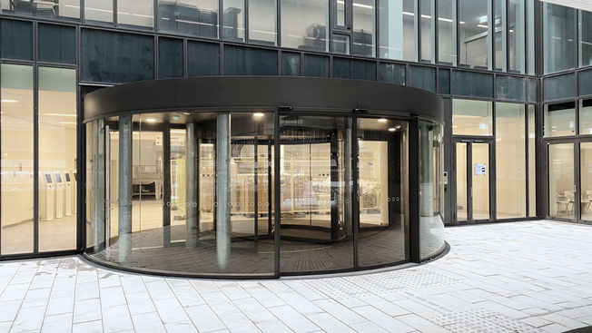 Rigshospitalet Dinamarca Uma porta de correr de vidro curva com automatismo Slimdrive SC é integrada na fachada de vidro inteligente em frente à porta giratória da entrada para pacientes.