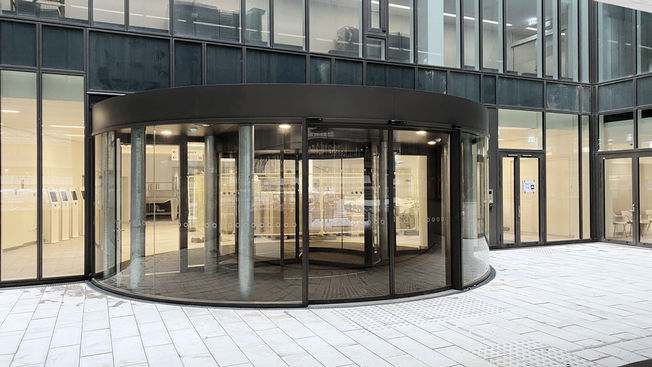 Rigshospitalet Danemark Une porte coulissante incurvée en verre avec automatisme de portes SC Slimdrive est intégrée dans la façade en verre intelligente devant la porte tournante de l'entrée pour patients.