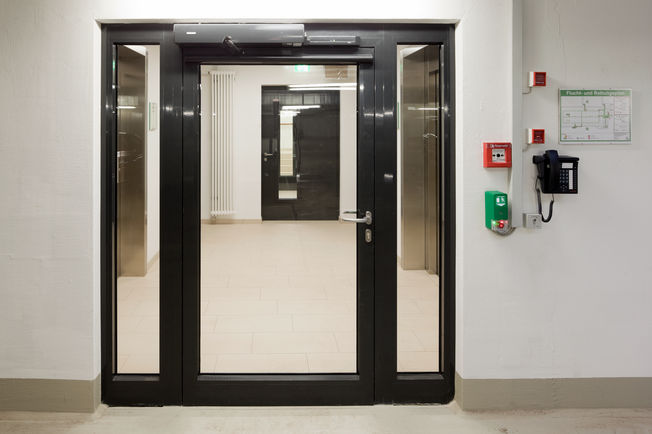 Swing door drive TSA 160 NT F-IS, GC334 sensor strip and the RWS TZ320 SN AP door control unit Electro-hydraulic swing door drive system for 2-leaf fire and smoke protection doors with integrated closing sequence control in the Augustinum retirement complex, Stuttgart.