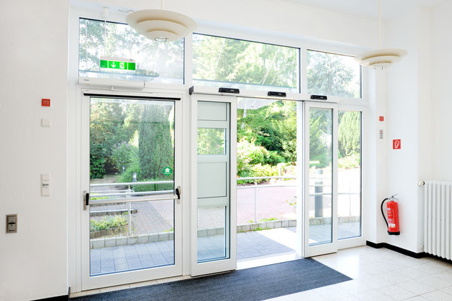 Automatic sliding door drive Slimdrive SL and automatic swing door drive Slimdrive EMD with guide rail and panic bar, installed at the Financial Academy Bonn Very smooth low-wear automatic linear sliding door system with low height and clear design line for optimum ease of access.