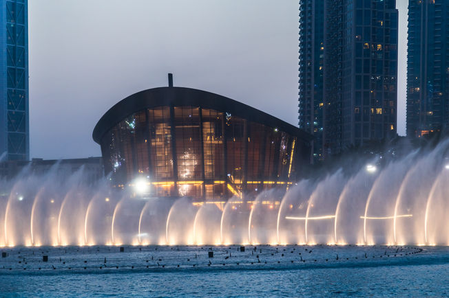 A Casa da Ópera do Dubai ao anoitecer vista da água.