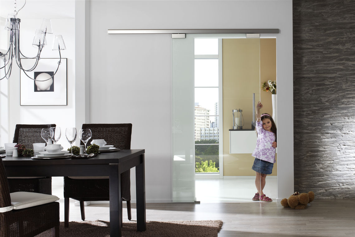 Il vetro gioca un ruolo di primo piano nell'interior design in stile moderno e nella separazione ambiente, creando trasparenza e ambienti aperti. Qui, un sistema di porta scorrevole manuale crea connessioni, luce e spazio.