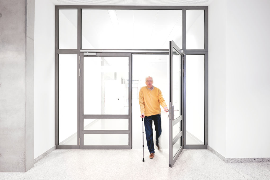 Bărbat în vârstă trecând printr-o ușă vitrată cu două canaturi