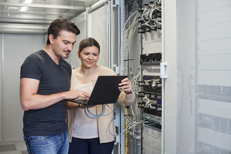 Empleados de GEZE delante de un armario eléctrico miran un ordenador portátil