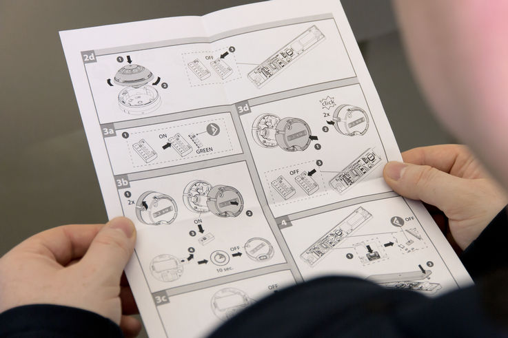 Two hands holding the assembly instructions for the GEZE FA GC 170 wireless extension kit for hold-open systems