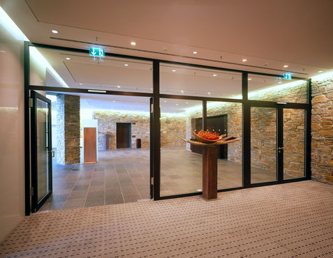 Korridorområde med romseparering av glass og åpen glassdør.