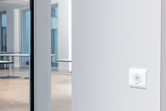 Безконтактна сенсорна кнопка від GEZE, встановлена на стіні поруч зі скляними розсувними дверима у будинку-інтернаті Fux Campagna.
