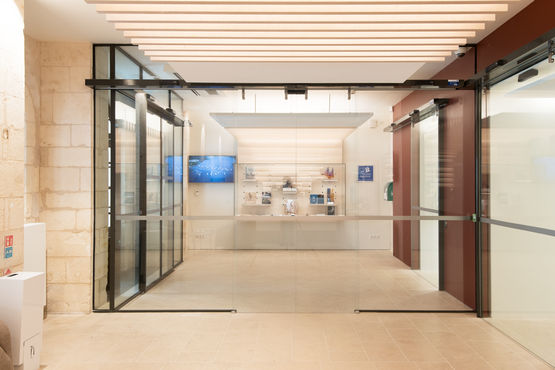 Der Empfangstresen liegt hinter einer automatischen Ganzglastür, die im Eingangsbereich des historischen Gebäudes für Barrierefreiheit sorgt.