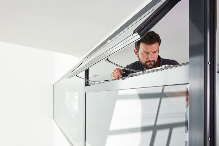 Ein Servicetechniker von GEZE begutachtet ein aufgekipptes Oberlicht-Fenster