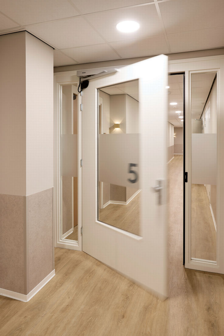 A half-open glass door with automatic drive units in a modern nursing home corridor.