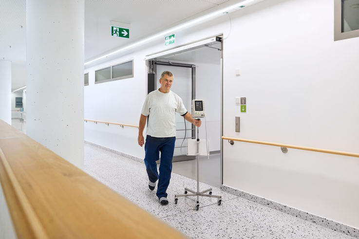 Patient mit Infusionstropf läuft durch einen Krankenhausflur.
