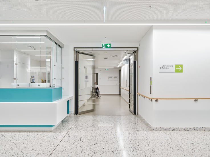 Ansicht eines Krankenhaus-Flurs, im Hintergrund ein Rollstuhlfahrer
