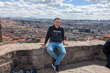 GEZE Trainee Jonas Sehmsdorf sitzt auf einer Mauer eines Aussichtspunkts hoch über einer Stadt in der Türkei.