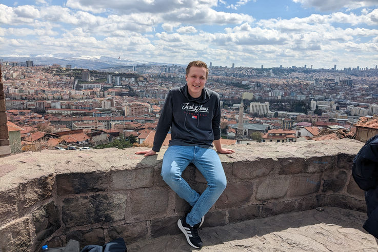 GEZE Trainee Jonas Sehmsdorf sitzt auf einer Mauer eines Aussichtspunkts hoch über einer Stadt in der Türkei.