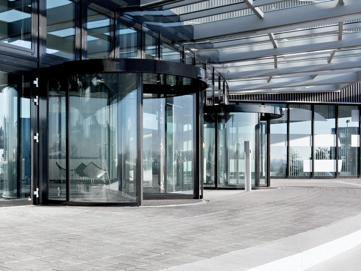 TSA 325 NT BO Automatic revolving door system for escape and rescue routes with breakout function. This function allows you to move the leaf and end caps in the direction of escape. The entrance to the building has plenty of natural light, the glass façades meet the highest design demands. There is an obstacle detection that stops the opening or closing process when an obstacle is detected by touch.