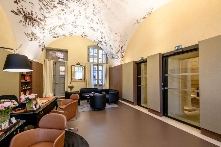 Hotellobby mit braunen und schwarzen Sesseln und Tischen und Glastüren rechts