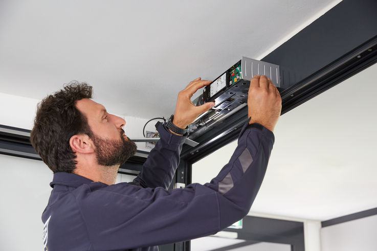 Ein GEZE Servicemitarbeiter baut einen Türschließer an einer Tür ein.